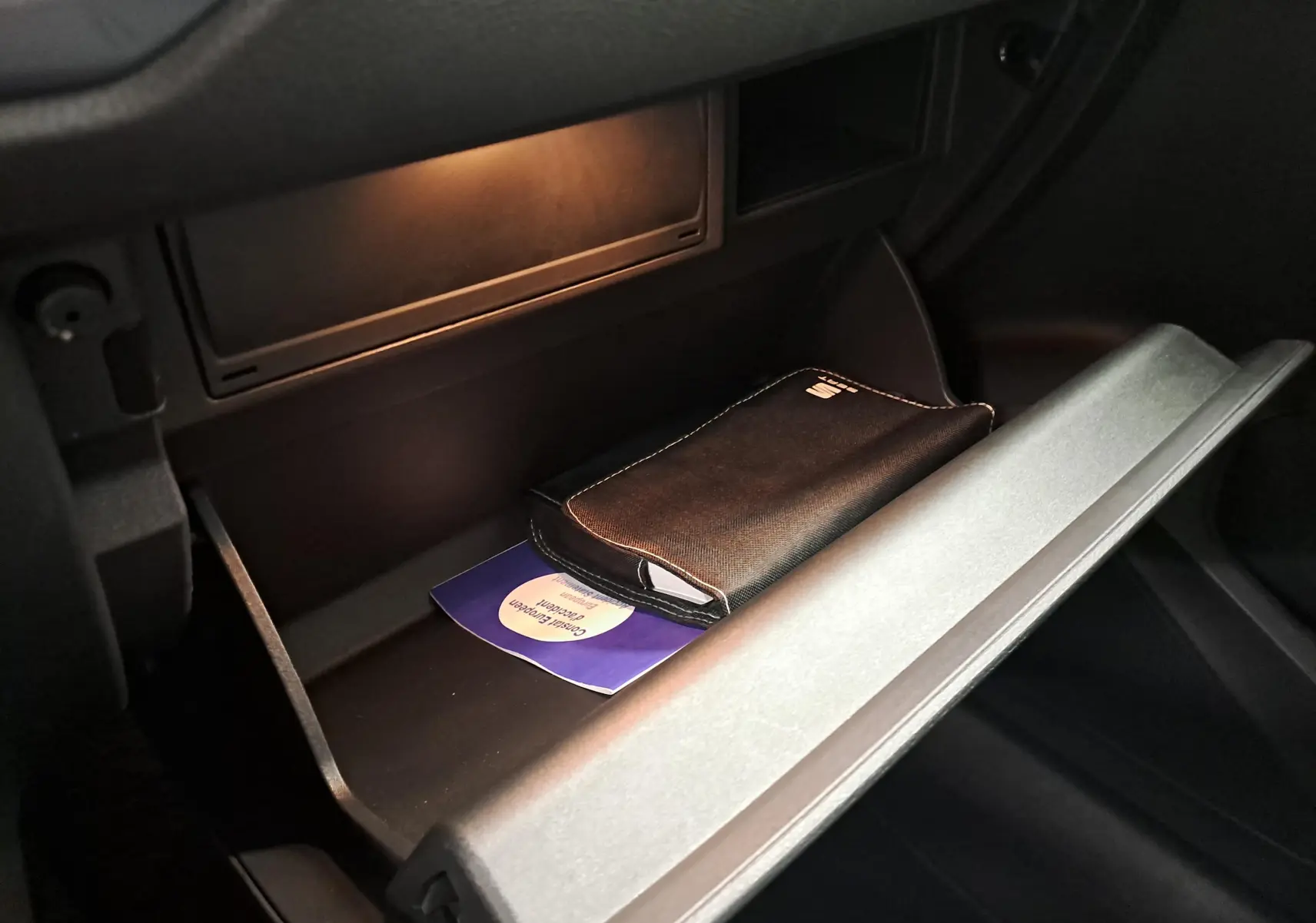 Gant de boîte à gants ouvert dans un SEAT Ateca 2023, intérieur noir avec éclairage doux et pochette noire visible.