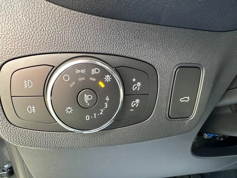 Gros plan sur le sélecteur de réglage des phares et bouton d'ouverture du coffre dans l'habitacle d'une Ford Puma 2023.
