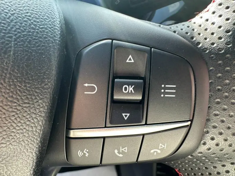 Gros plan sur les commandes multifonctions noires du volant perforé du Ford Puma 2023 gris Solar Métallisée.