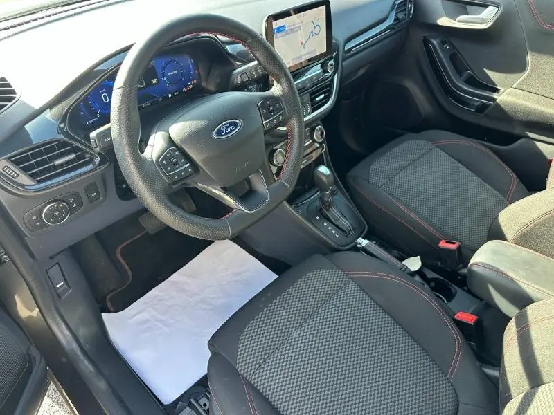Vue intérieure côté conducteur du Ford Puma 2023, volant multifonction, sièges tissu noir avec surpiqûres rouges et écran tactile central.