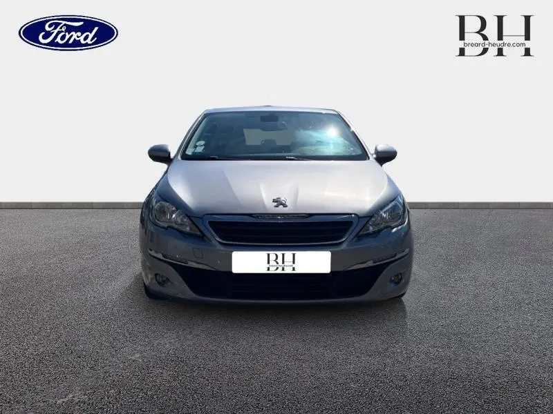 Vue frontale d'une Peugeot 308 gris Artense avec calandre noire et phares halogènes visibles.