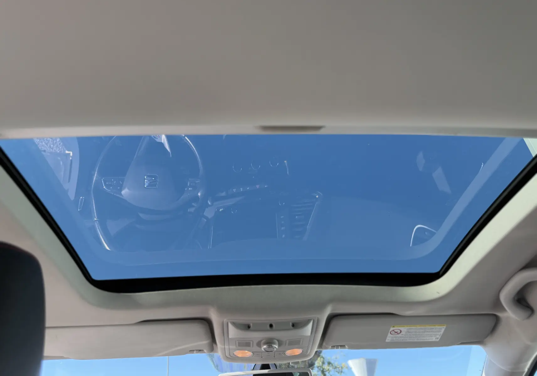 Vue intérieure du toit ouvrant panoramique du SEAT Leon blanc 2014, avec reflet du tableau de bord et ciel bleu visible.