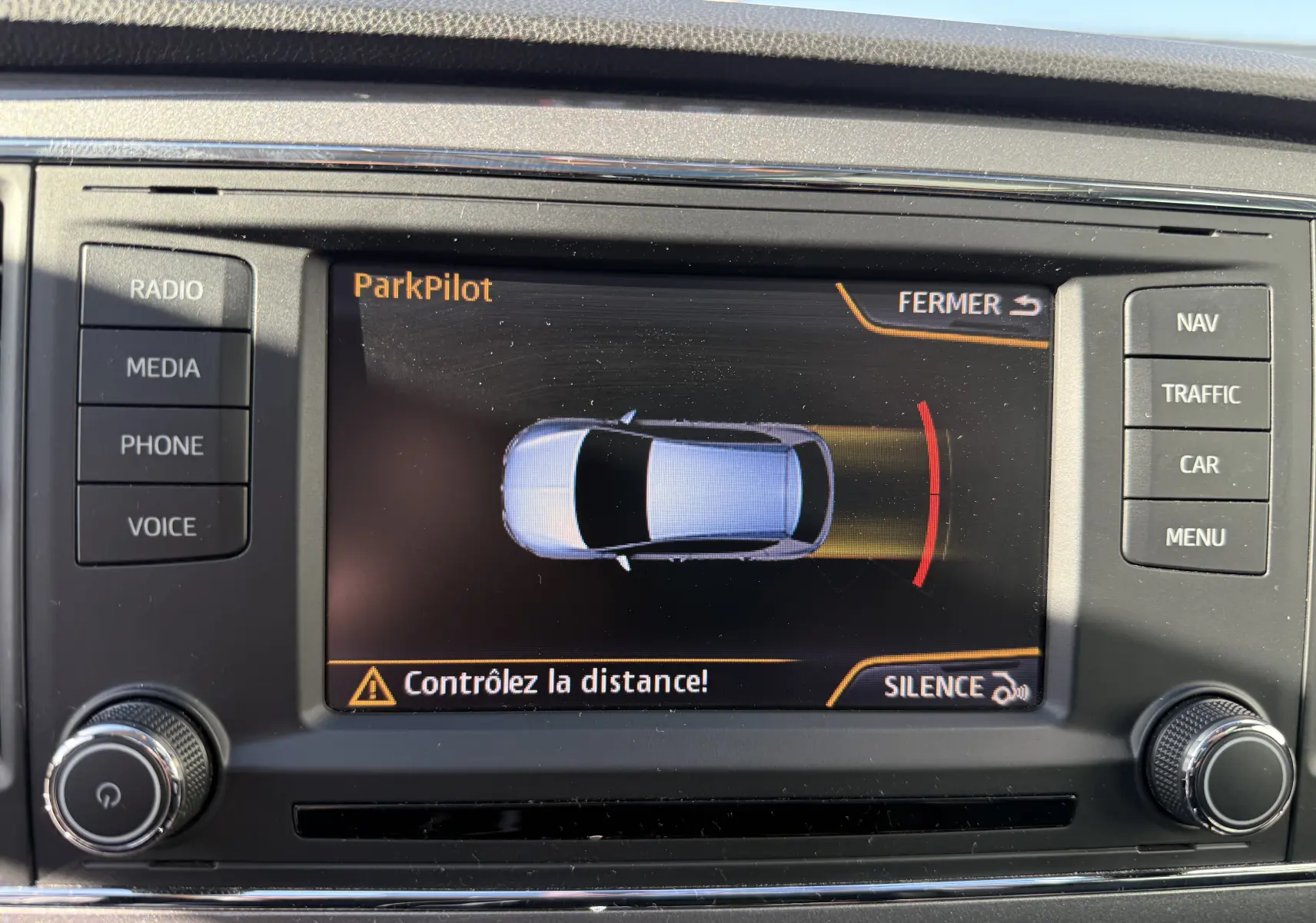 Écran central du système ParkPilot montrant une SEAT Leon blanche vue de dessus avec alerte de distance au stationnement.