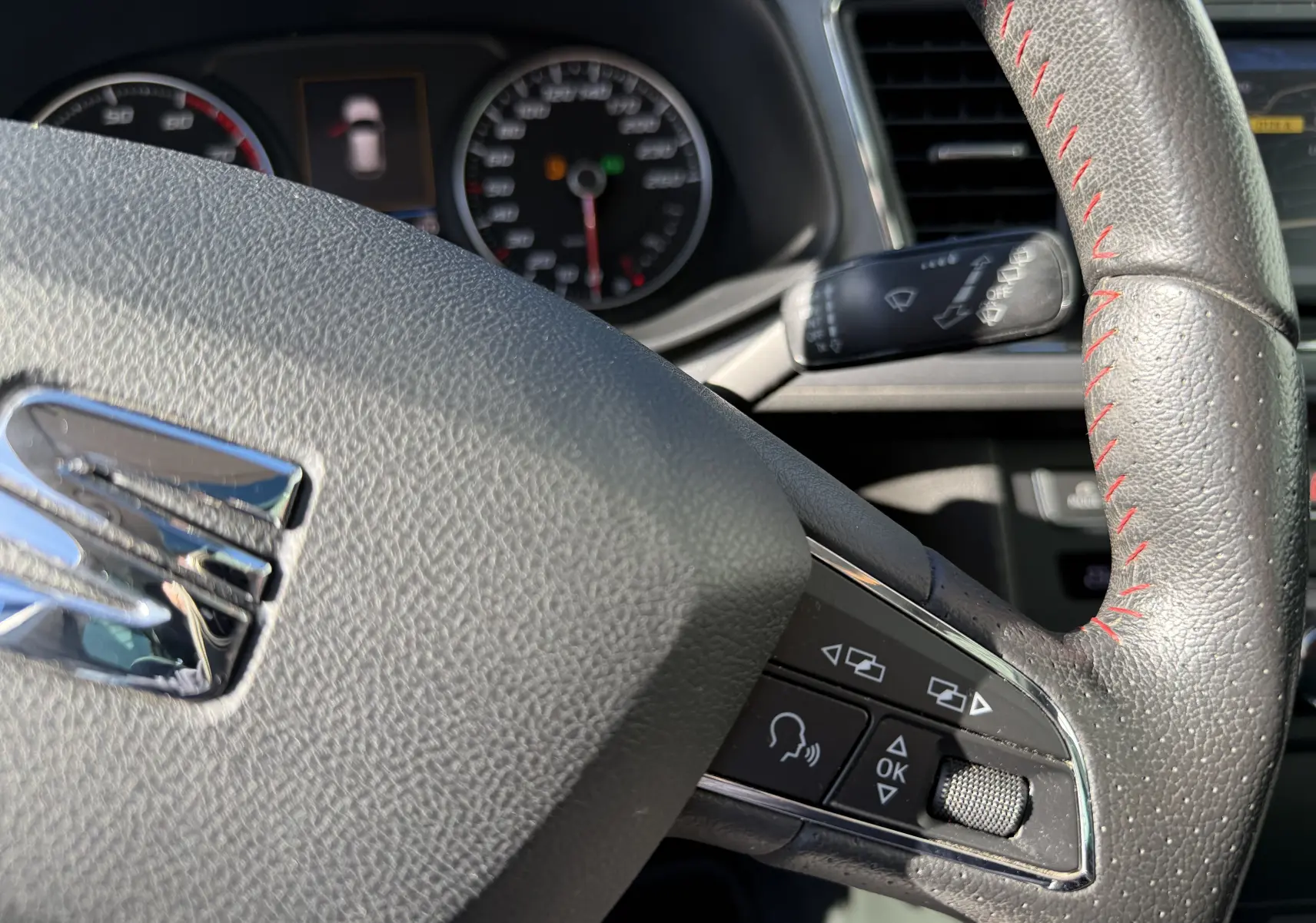 Gros plan sur le volant en cuir noir avec surpiqûres rouges du SEAT LEON 1.8 TFSI 180 FR, montrant les commandes intégrées.