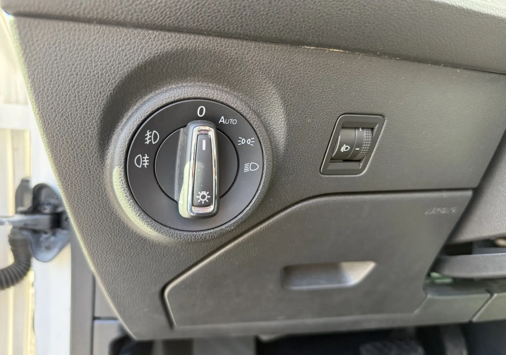 Gros plan sur le bouton de commande des phares et le réglage d’intensité lumineuse dans un SEAT Leon blanc 2014, côté conducteur.