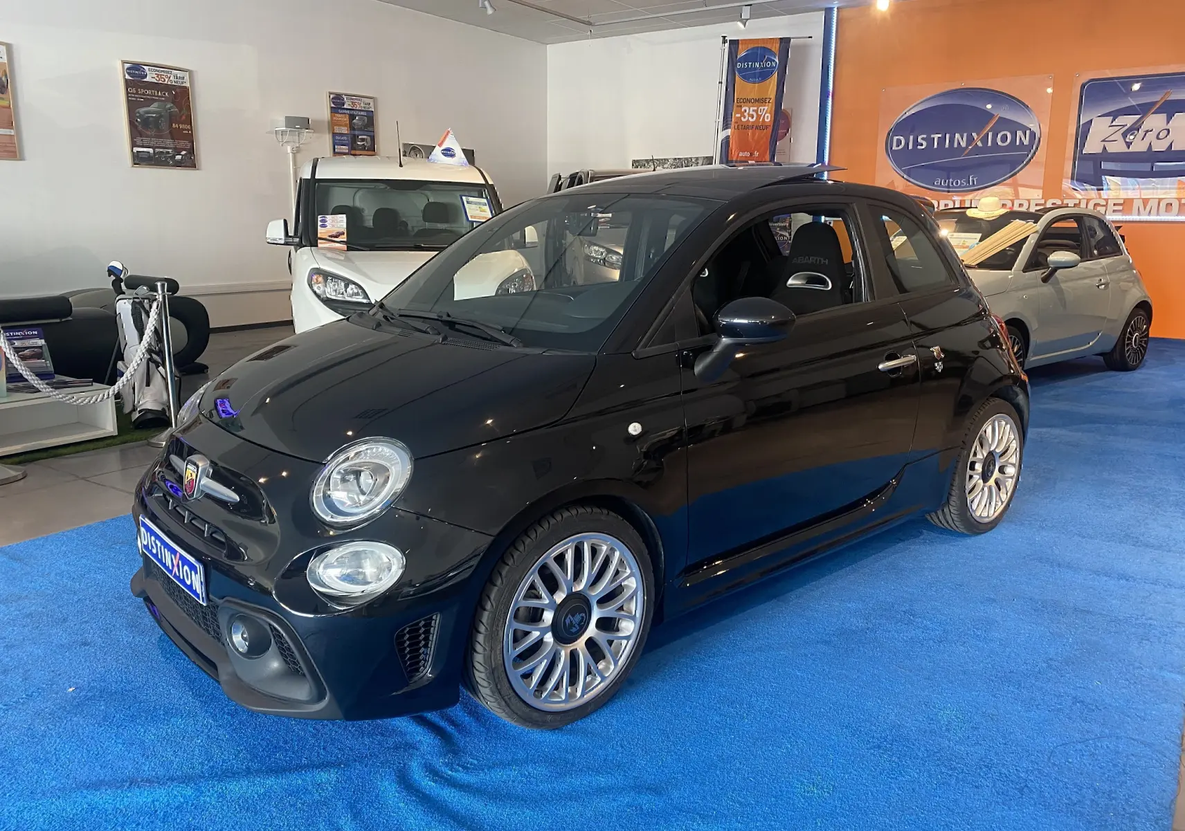 Vue 3/4 avant droite d'une ABARTH 595 noire avec jantes alu 17 pouces et intérieur sport visible en showroom.