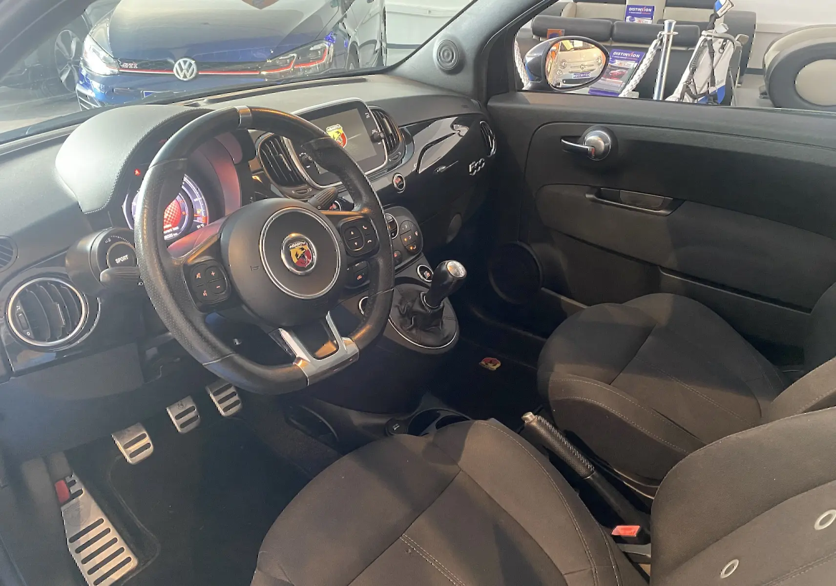 Vue intérieure côté conducteur de l'Abarth 595 noire, volant sport, levier de vitesse manuel et tableau de bord moderne.