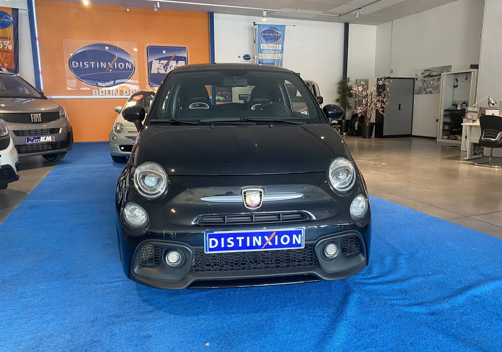 Vue frontale d'une ABARTH 595 noire avec logo distinctif et plaque "DISTINXION" en concession lumineuse.