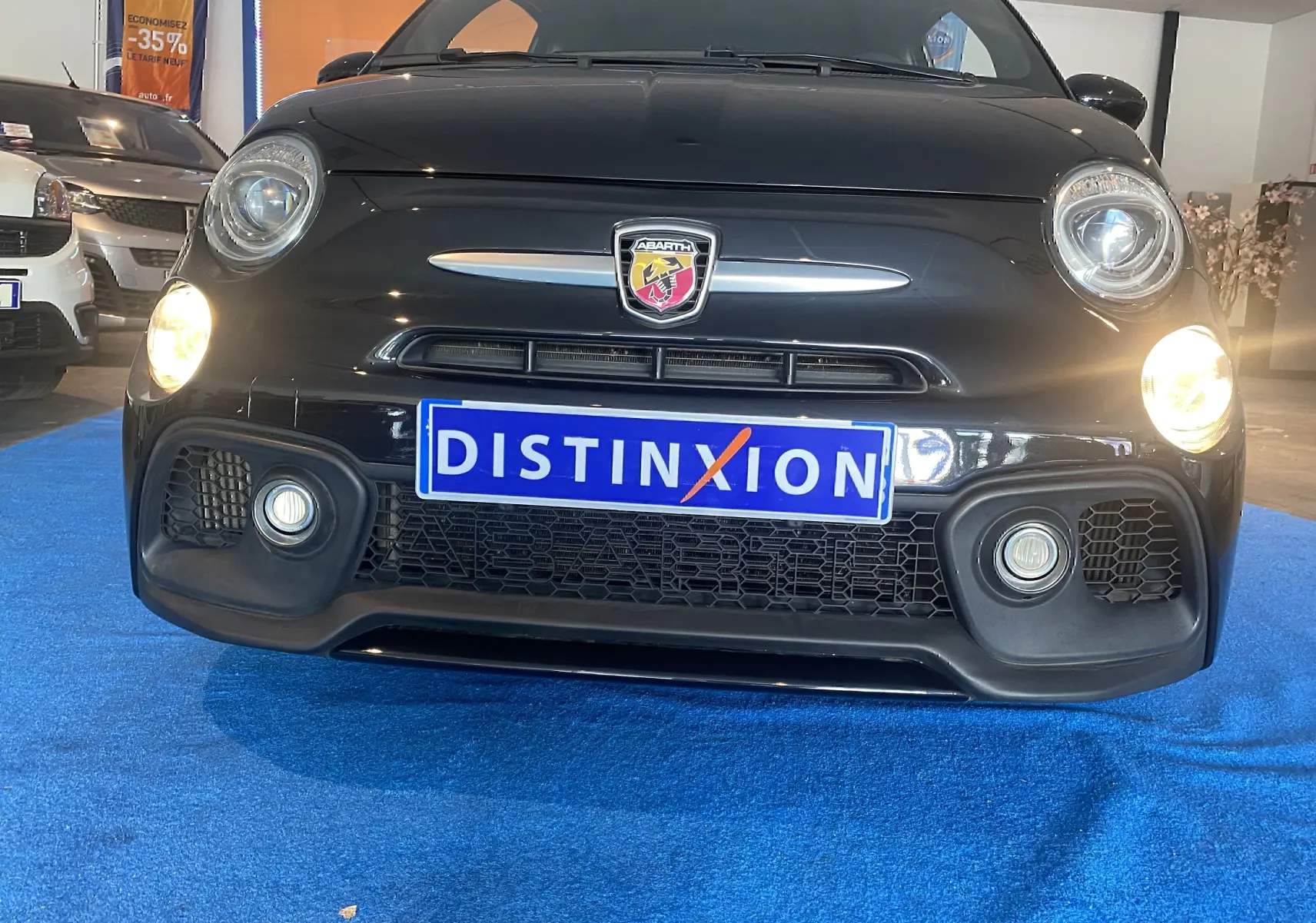 Vue frontale rapprochée de l'Abarth 595 noire avec phares allumés et logo Abarth bien visible sur calandre.