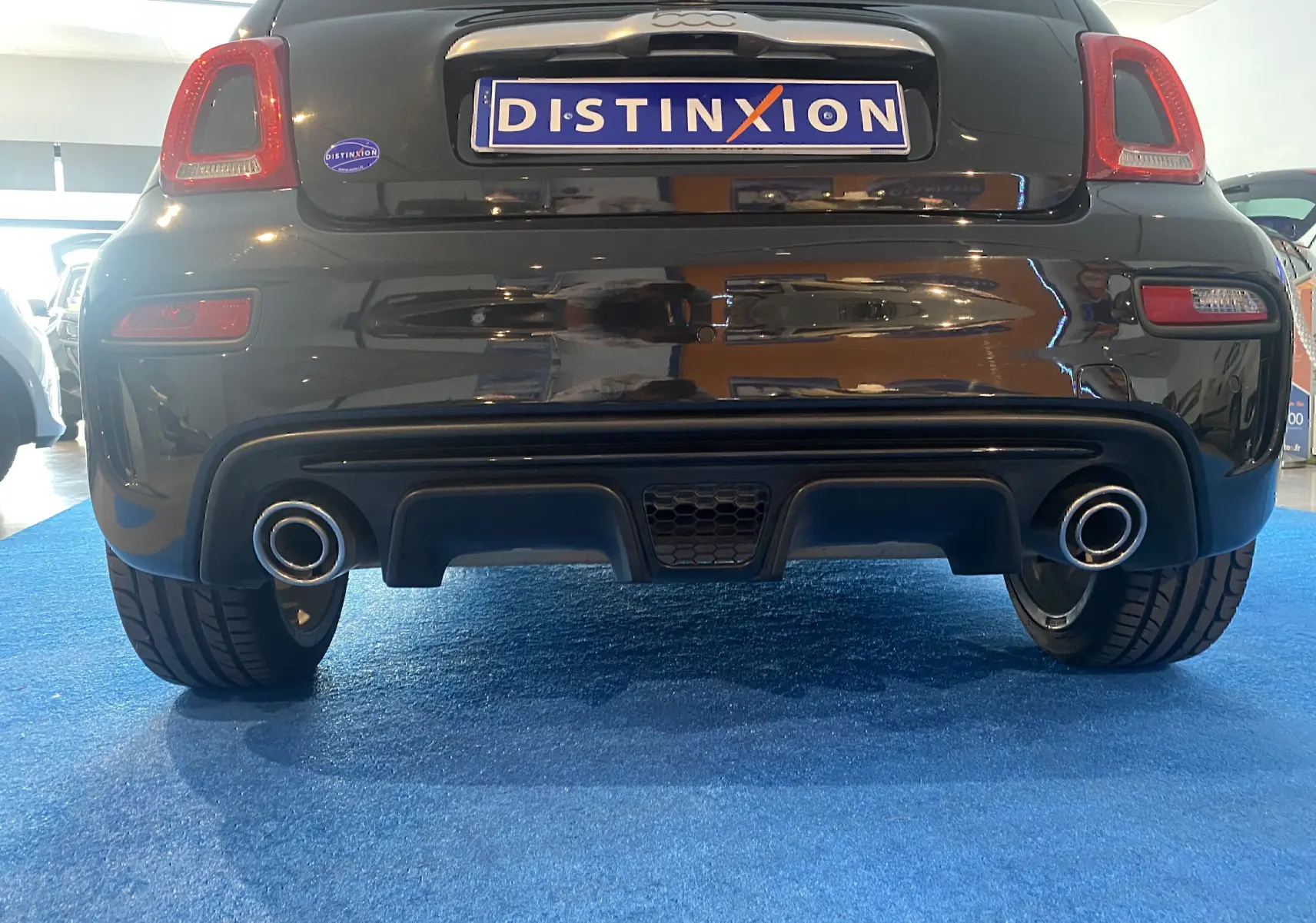Vue arrière basse d'une ABARTH 595 noire de 2018 avec double sortie d'échappement et plaque Distinxion visible.