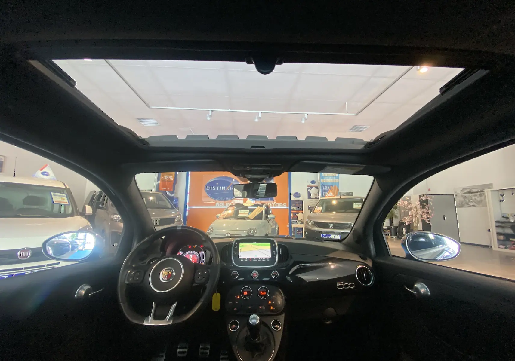 Vue intérieure du toit ouvrant électrique et tableau de bord noir de l'Abarth 595 avec écran GPS allumé.