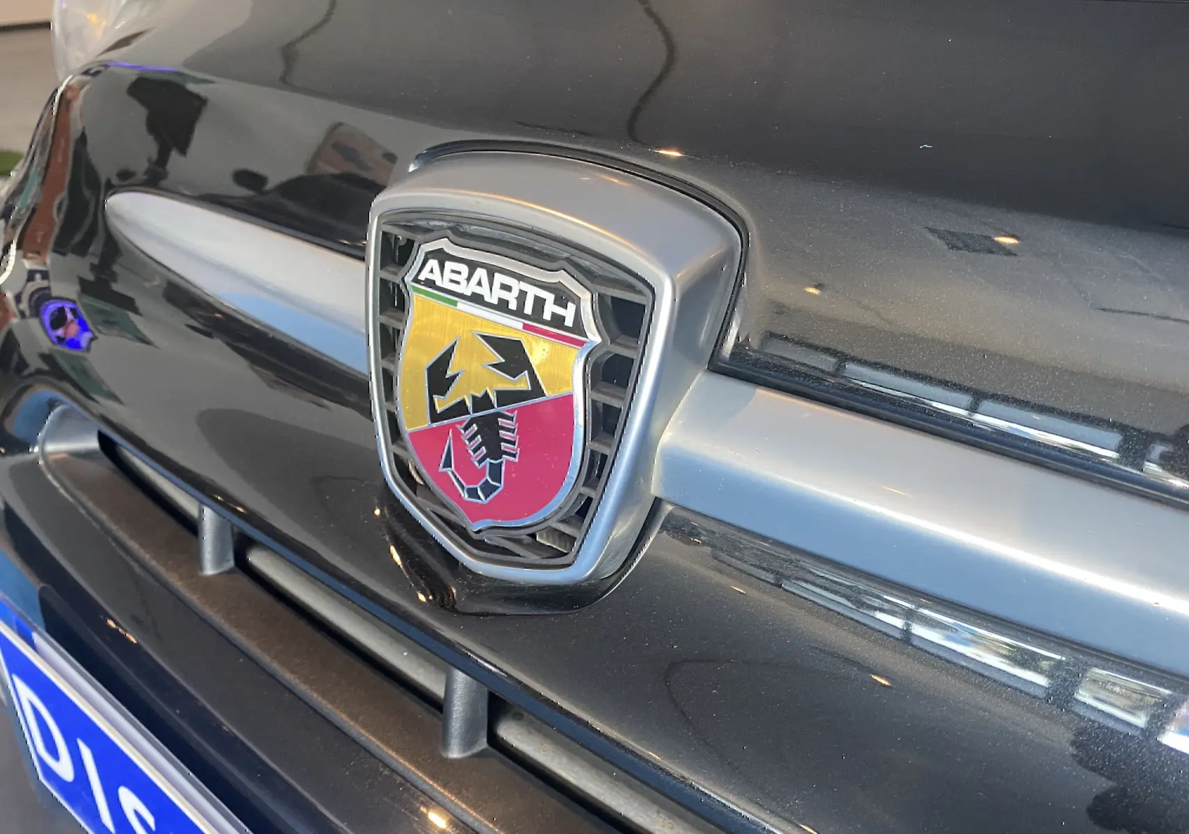 Gros plan sur l'emblème Abarth noir et rouge sur la calandre avant d'une ABARTH 595 noire.