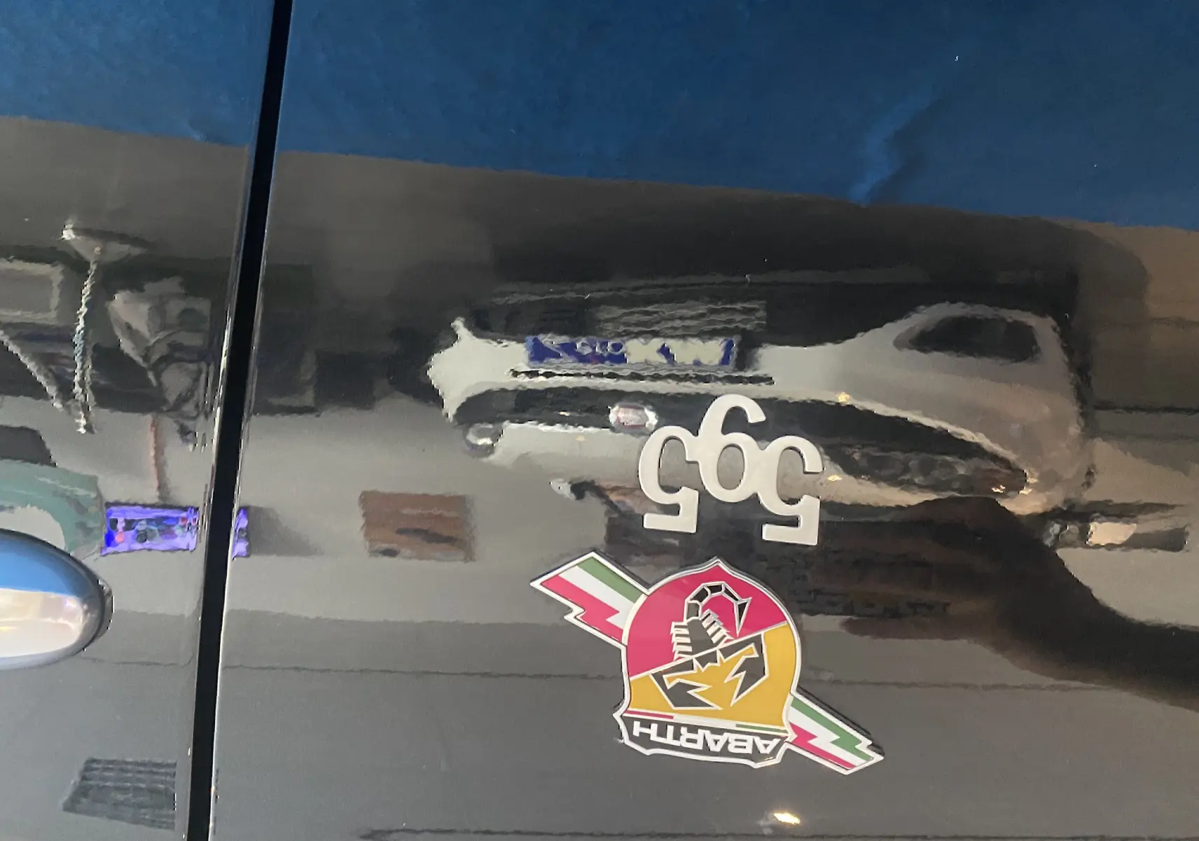 Gros plan sur la porte noire d'une Abarth 595 avec logo scorpion coloré et badge 595 blanc.