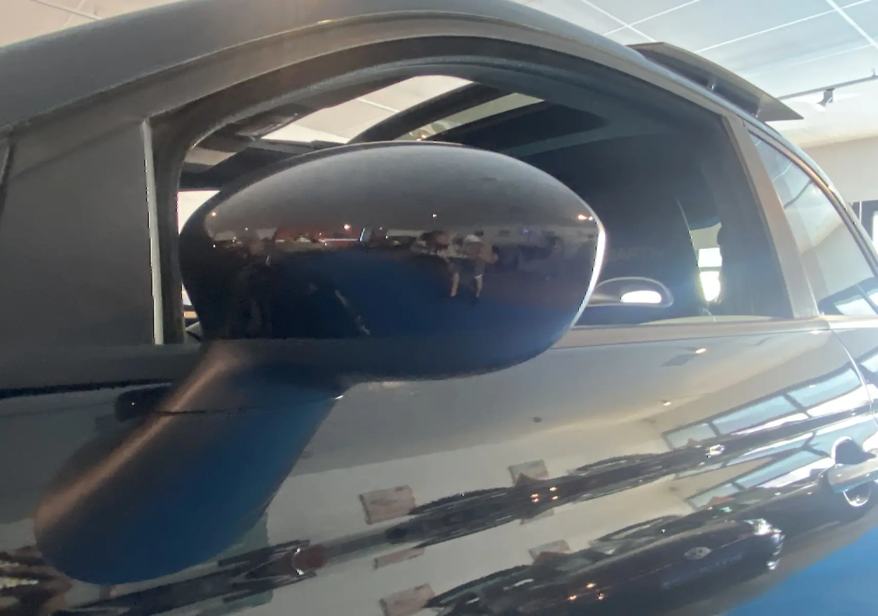 Rétroviseur noir en gros plan sur le côté gauche d'une ABARTH 595 noire avec toit ouvrant visible en intérieur.