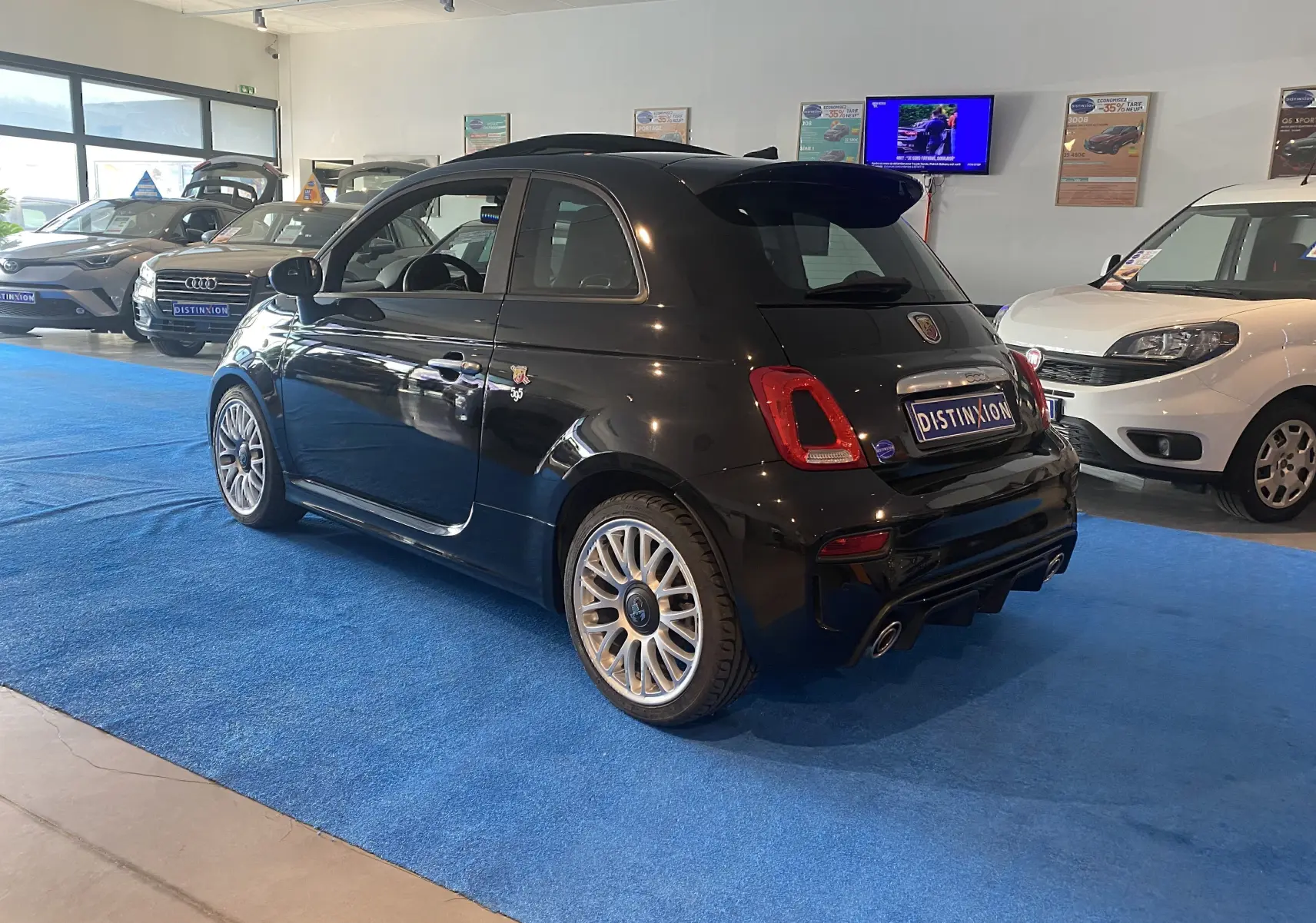 ABARTH 595 noir vu de 3/4 arrière droit dans un showroom, avec jantes alu 17 pouces et toit ouvrant fermé.