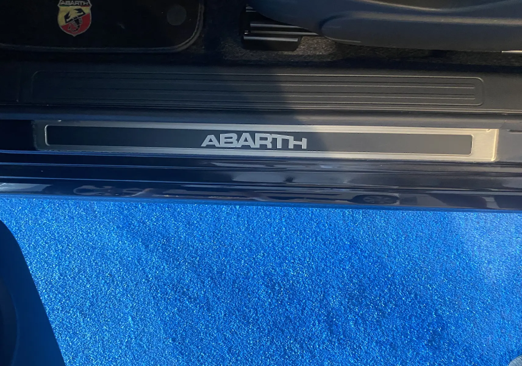 Gros plan sur la plaque de seuil de porte ABARTH noire avec logo Abarth visible en haut à gauche.