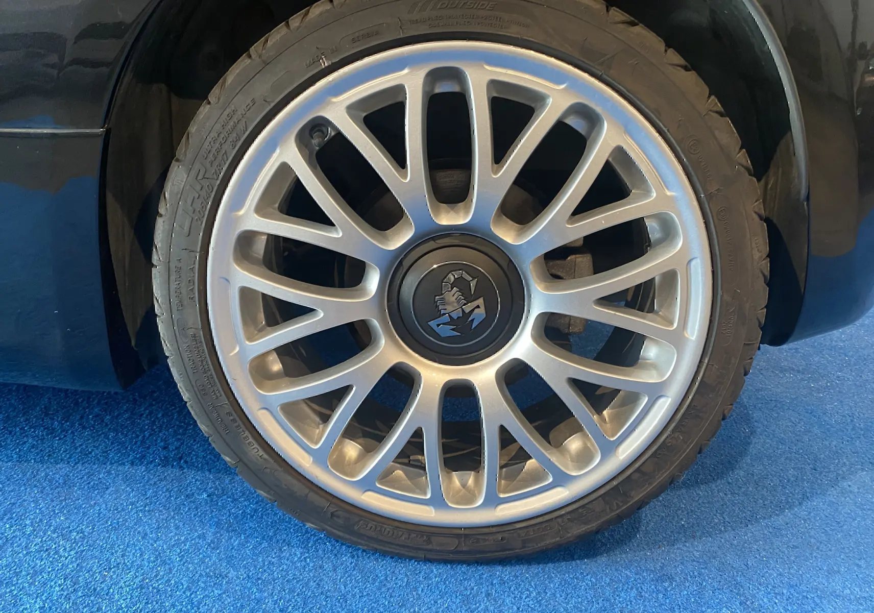 Gros plan sur la jante alu 17 pouces argentée avec logo scorpion de la roue avant droite d'une ABARTH 595 noire.