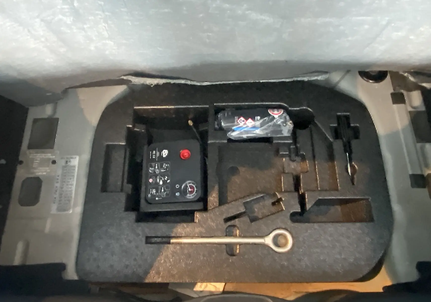 Gros plan sur le compartiment à outils et kit de réparation sous le coffre de l'Abarth 595 noir de 2018.