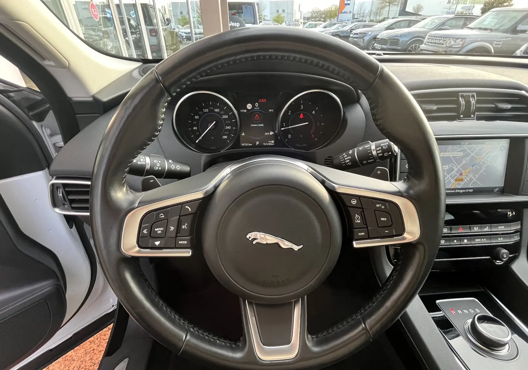 Vue intérieure centrée sur le volant cuir noir du Jaguar F-PACE blanc 2018 avec tableau de bord et écran GPS visible.