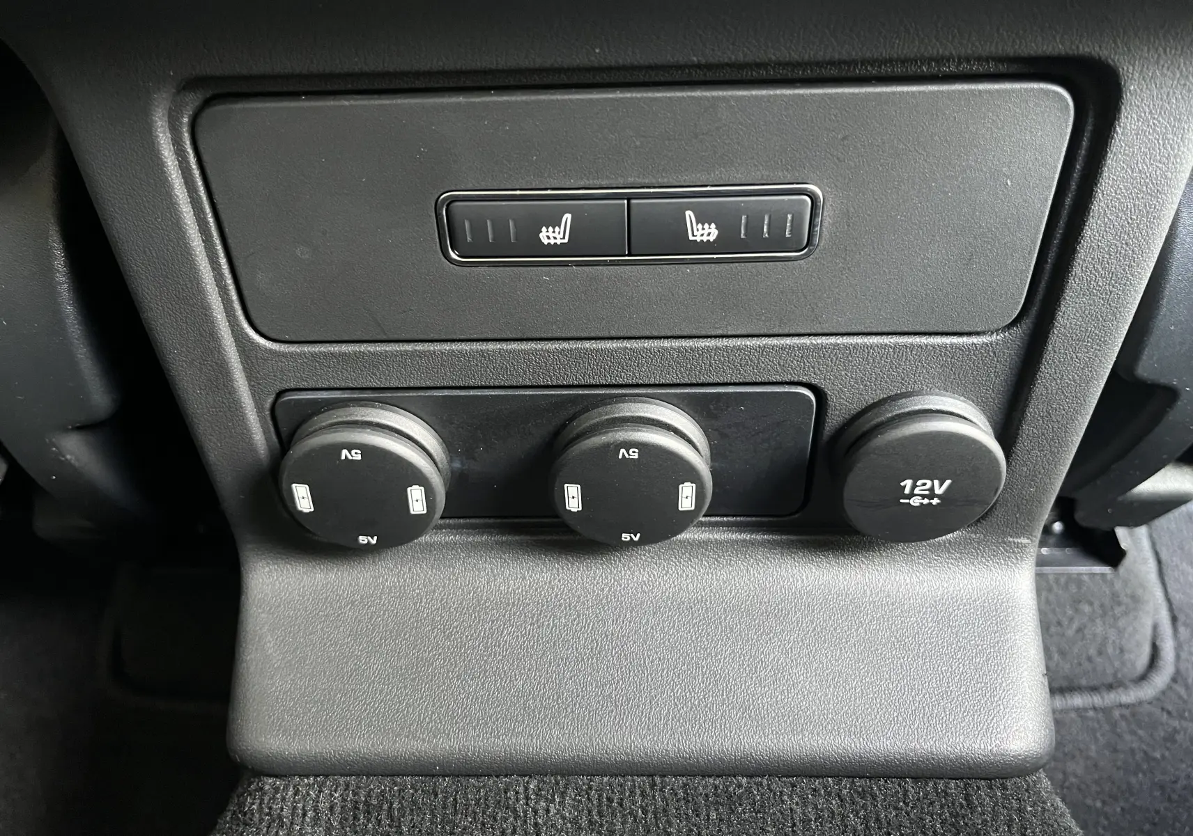 Gros plan sur les commandes de sièges chauffants et prises 5V/12V à l'arrière d'un Jaguar F-PACE blanc 2018.