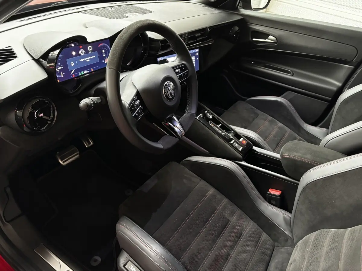 Vue intérieure côté conducteur de l'Alfa Romeo Junior 2024, sièges Sabelt noirs avec surpiqûres rouges et tableau de bord digital.
