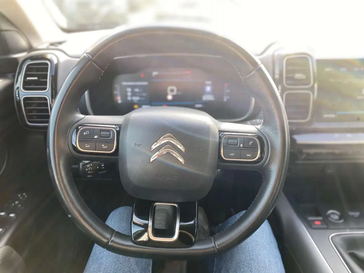 Vue intérieure centrée sur le volant cuir noir de la Citroën C5 Aircross 2021 avec tableau de bord numérique flou en arrière-plan.