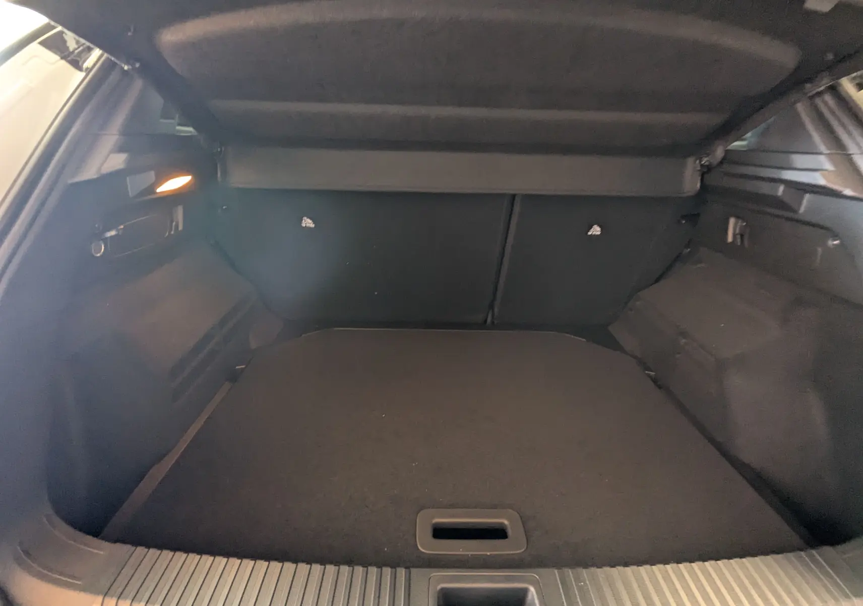 Coffre ouvert vu de l'arrière du Renault Austral E-Tech blanc nacré avec intérieur noir et cache-bagages déployé.