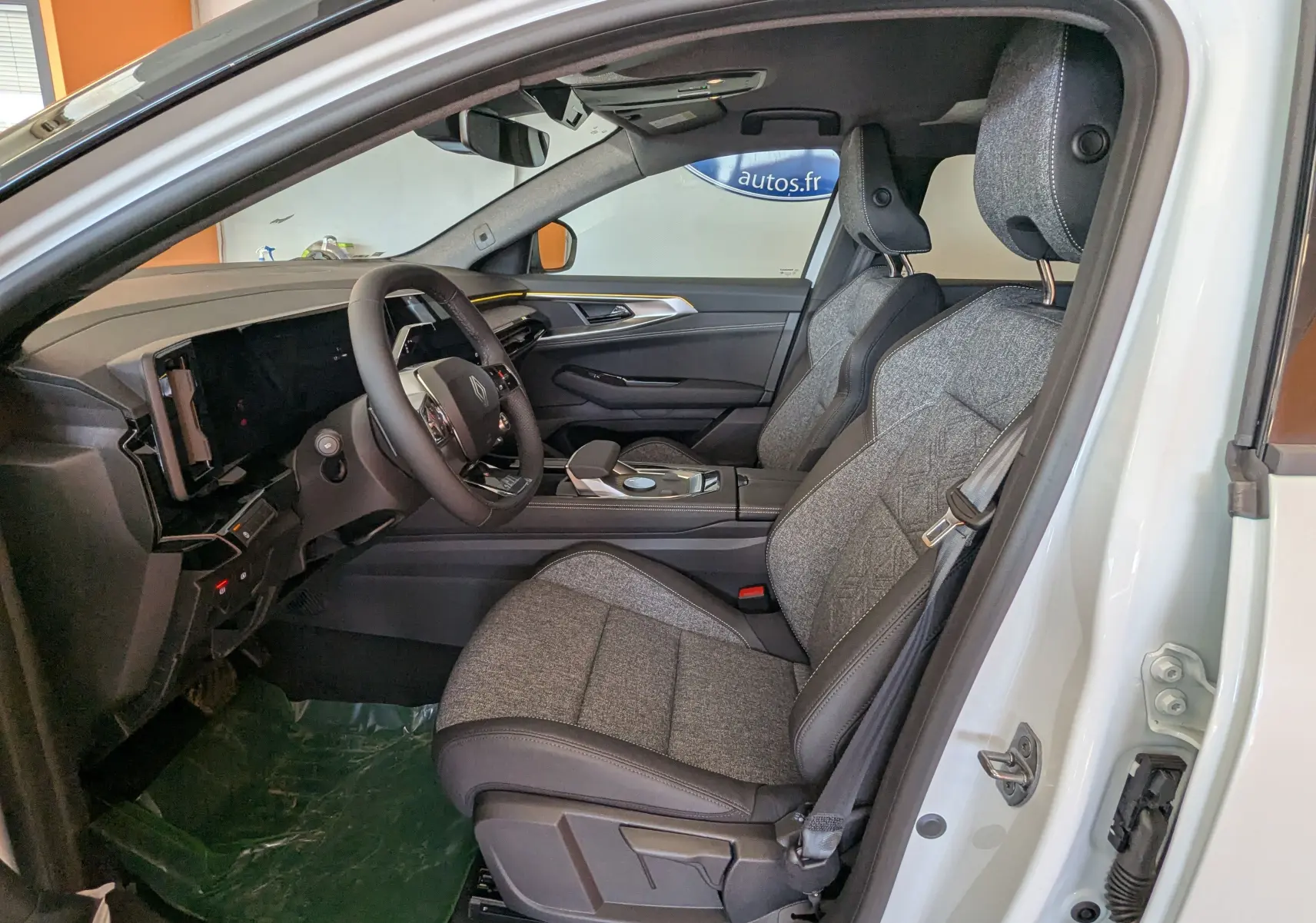 Vue intérieure côté conducteur du Renault Austral E-Tech blanc nacré, sièges tissu gris nuancé et tableau de bord moderne.