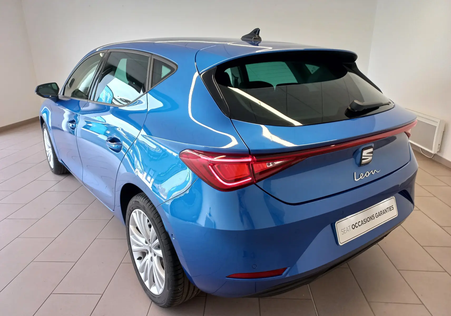 Vue 3/4 arrière gauche d'une SEAT Leon 2025 bleu saphir avec vitres arrière surteintées et rétroviseurs rabattables.