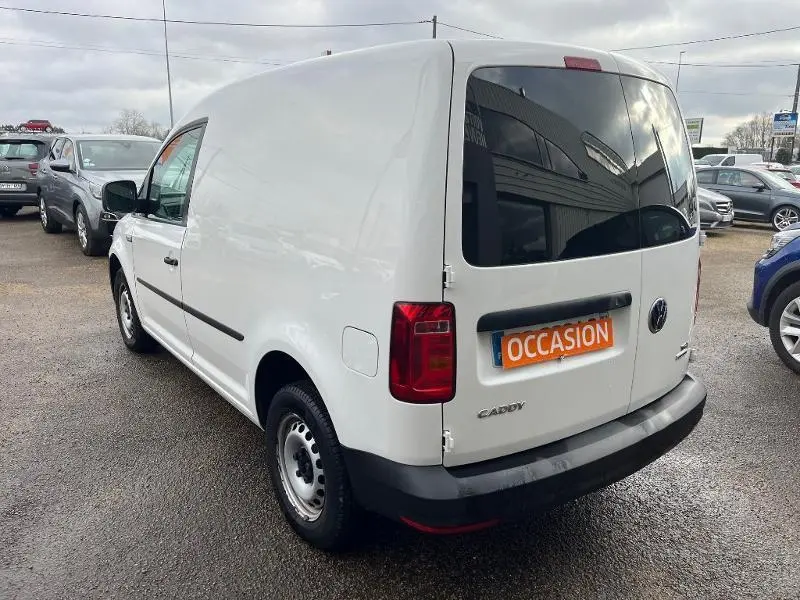 Vue 3/4 arrière droite d'un Volkswagen Caddy Van blanc Candy avec portes arrière vitrées et plaque "OCCASION" visible.