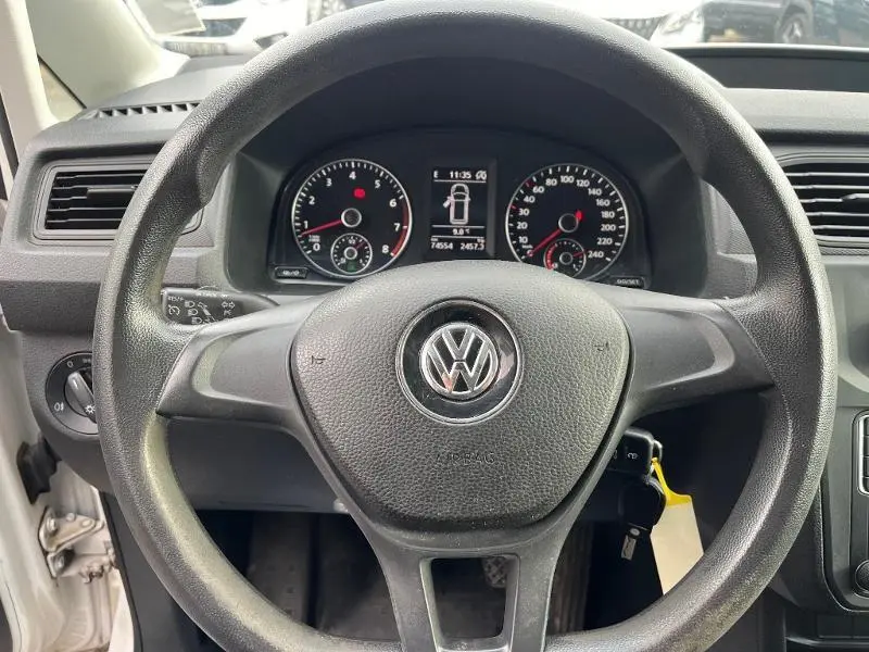 Vue rapprochée du volant noir et du tableau de bord du Volkswagen Caddy Van blanc, affichage multifonction visible.