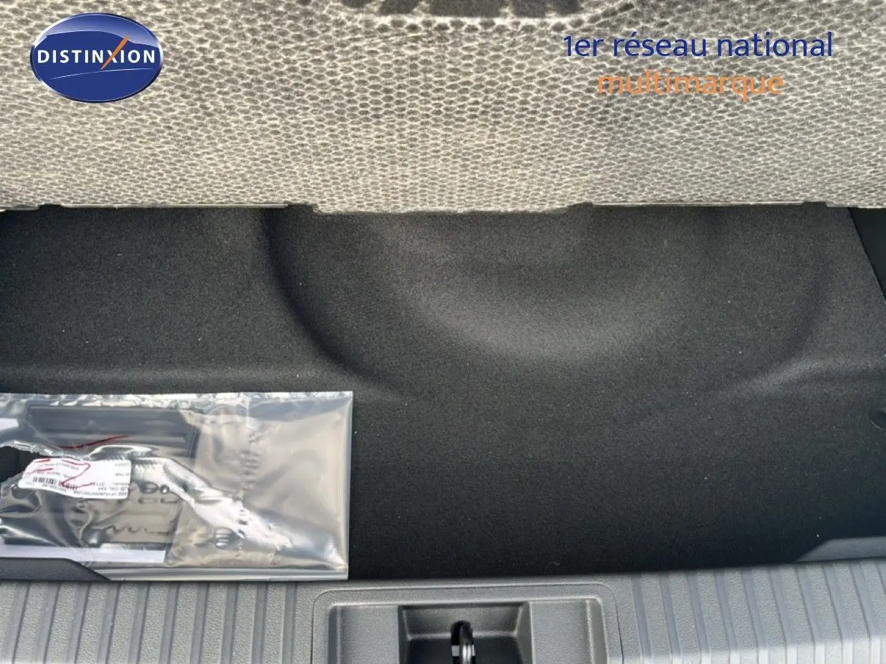 Vue du coffre arrière d'une Renault Symbioz blanc nacré, montrant le tapis noir et un kit d'accessoires emballé.