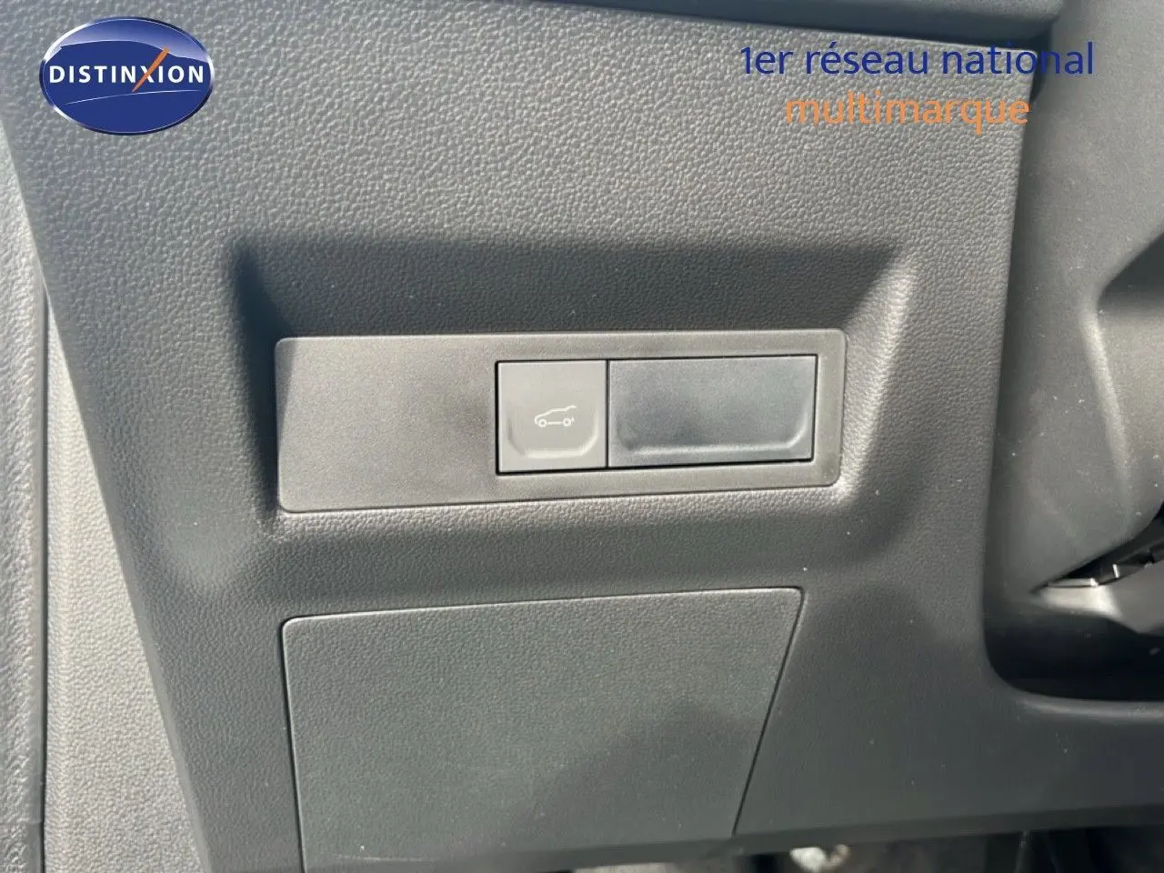 Détail du bouton d'ouverture du coffre sur la planche de bord noire d'une Renault Symbioz blanche nacrée.