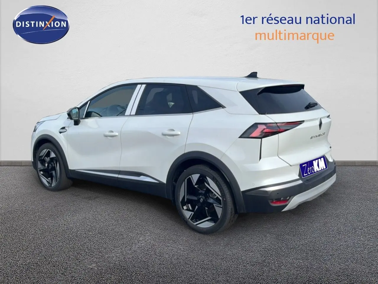 Renault Symbioz blanc nacré métal en vue 3/4 arrière droit, avec jantes noires et feux arrière LED distinctifs.