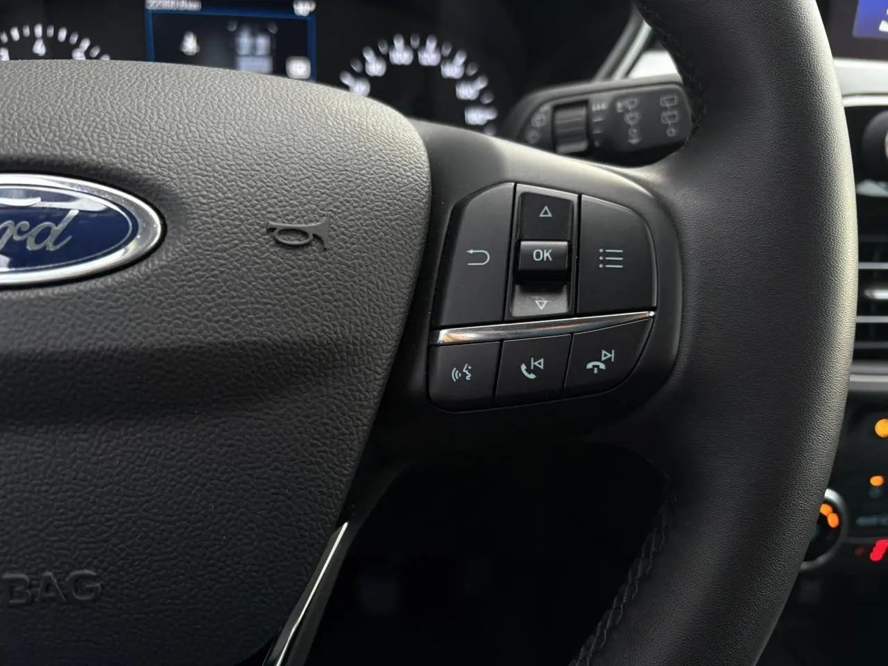 Gros plan sur le volant cuir noir du Ford Kuga 2024, avec commandes multifonctions et logo Ford visible au centre.