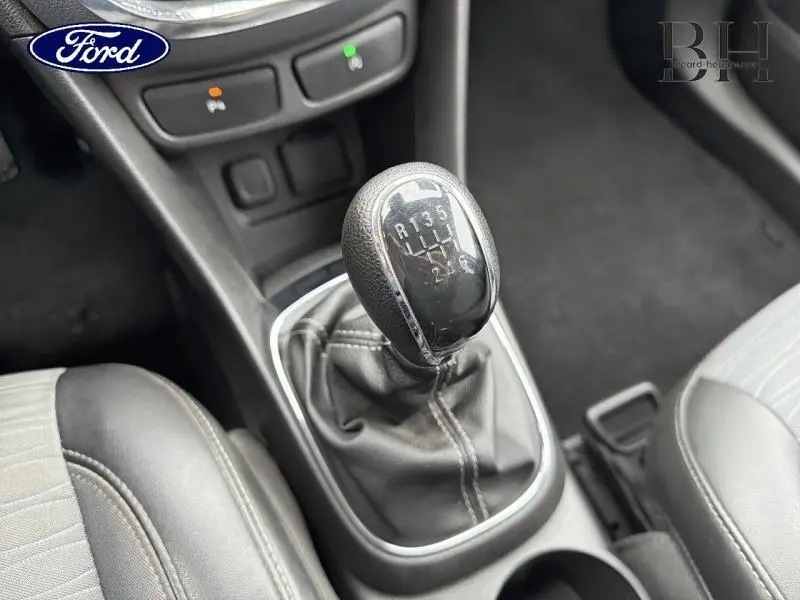 Gros plan sur le levier de vitesses manuel noir dans l’habitacle, entouré de sièges gris et console centrale.