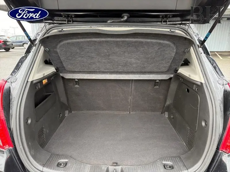 Coffre ouvert vu de l'arrière d'un Opel Mokka noir carbone, montrant l'espace de chargement et la tablette cache-bagages.