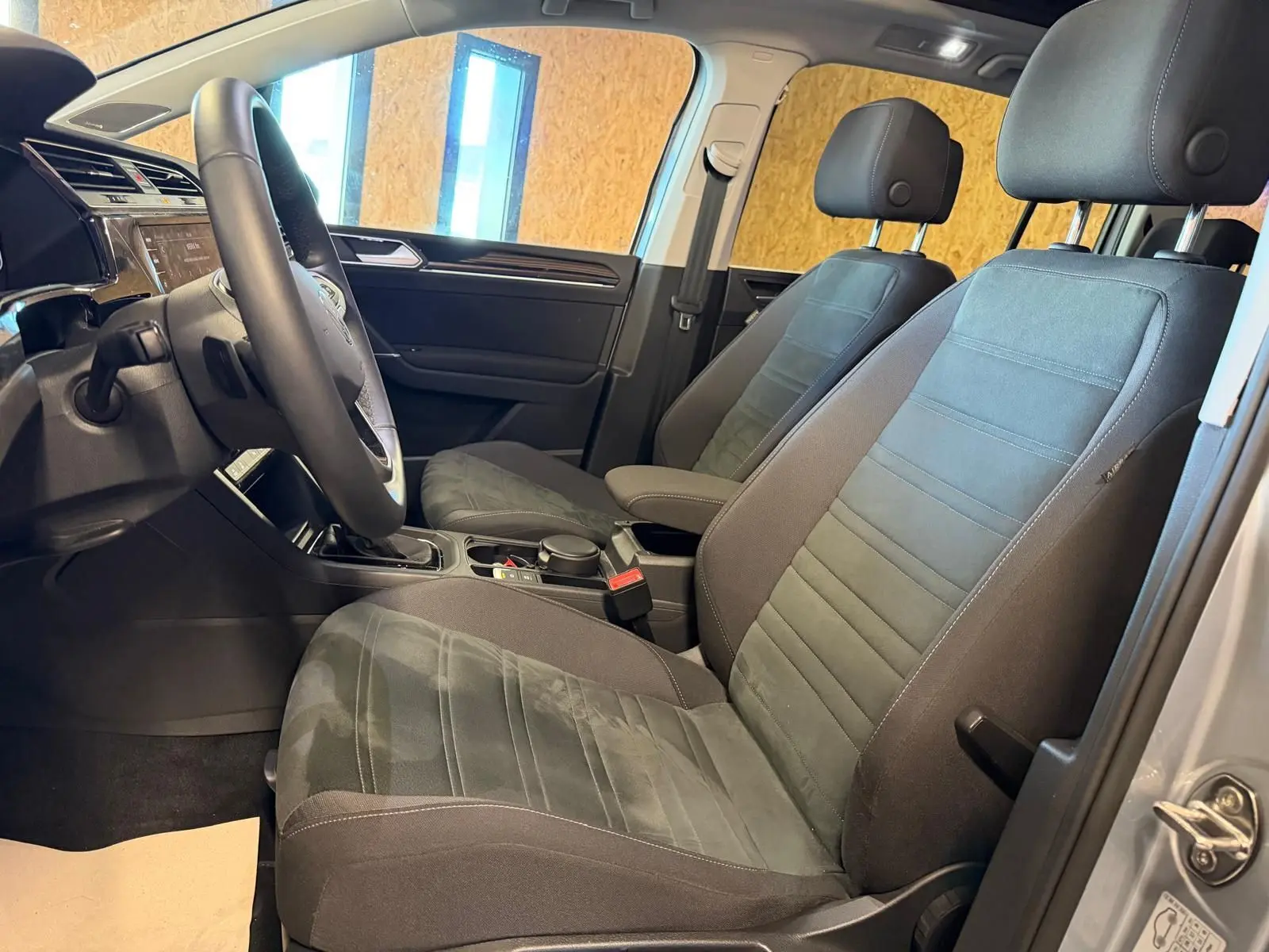 Vue intérieure côté conducteur du Volkswagen Touran gris 2025, montrant sièges avant et volant cuir multifonctions.