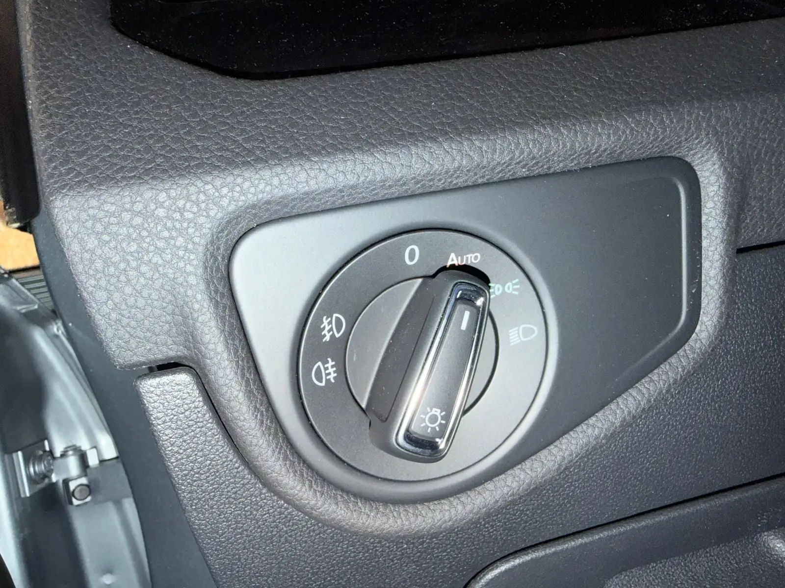 Gros plan sur le bouton de commande des phares dans un Volkswagen Touran gris, intérieur côté gauche.