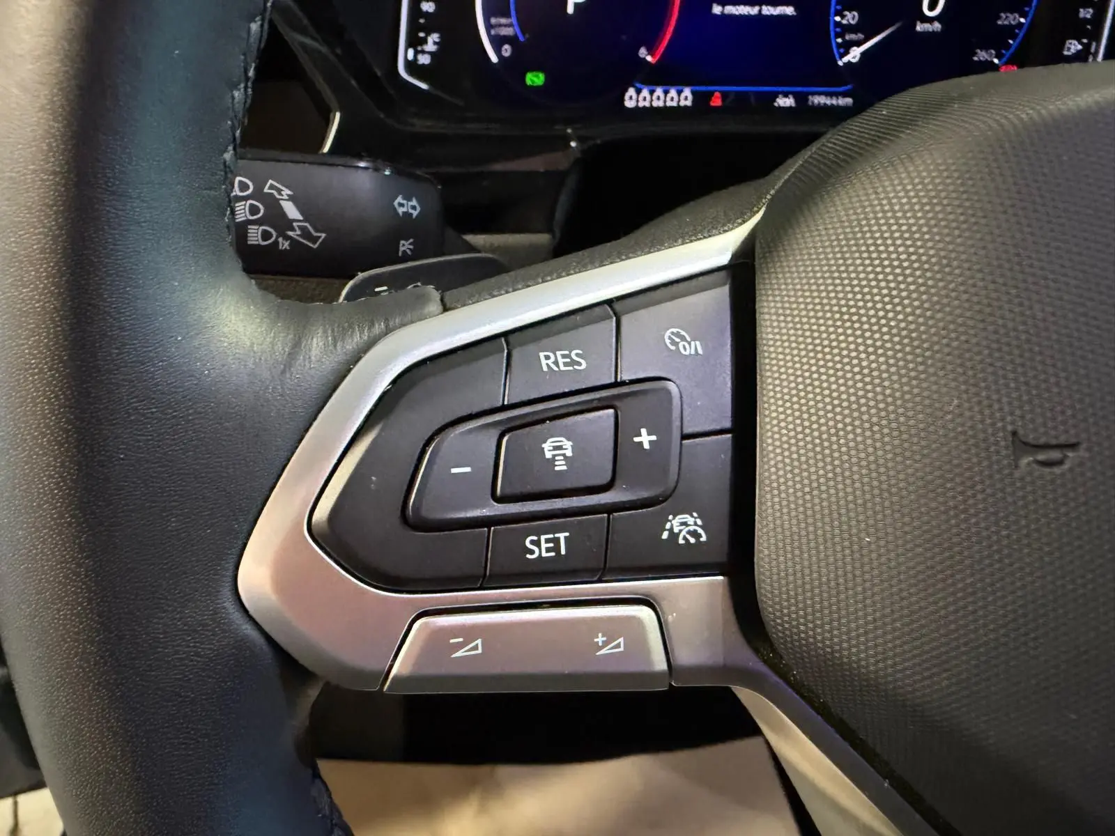 Gros plan sur les commandes du volant cuir noir du Volkswagen Touran 2025, avec régulateur de vitesse et aides à la conduite.