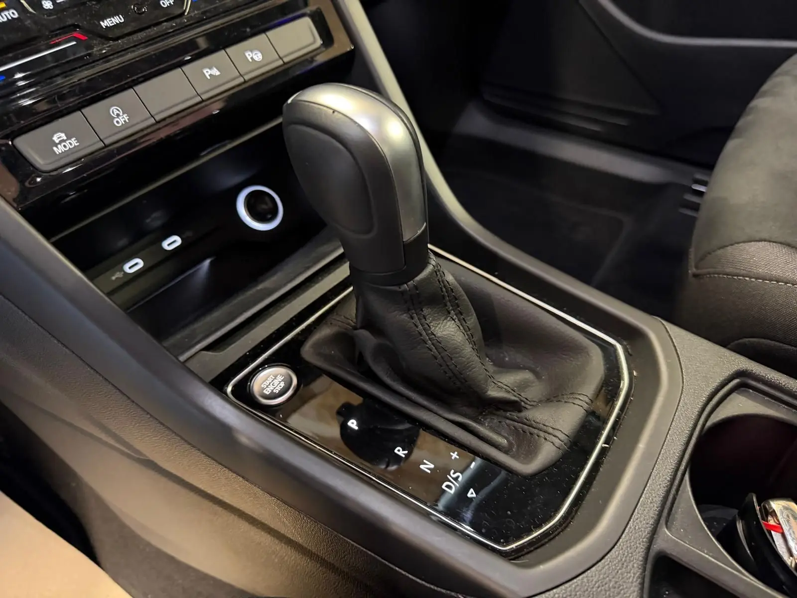 Gros plan sur la commande de la boîte automatique noire et cuir dans l’habitacle du Volkswagen Touran gris.