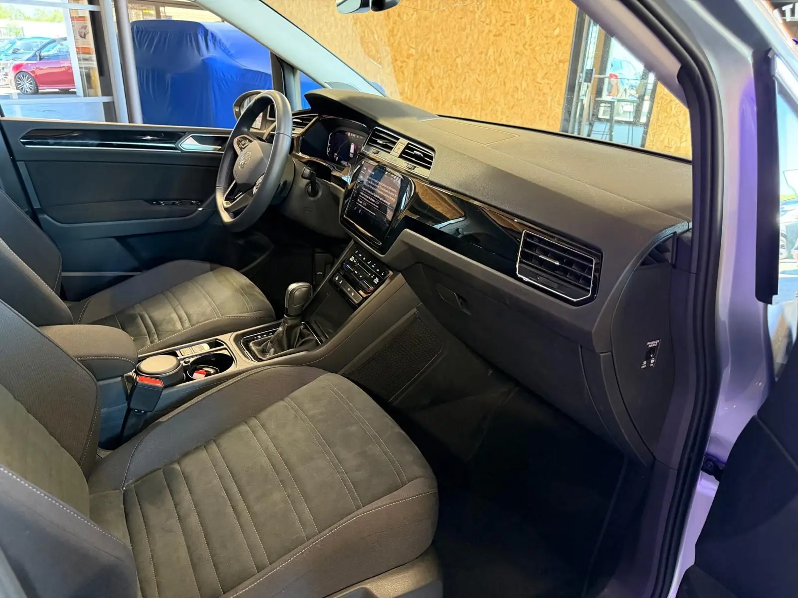 Vue intérieure côté conducteur du Volkswagen Touran gris 2025, mettant en valeur le tableau de bord et la console centrale moderne.