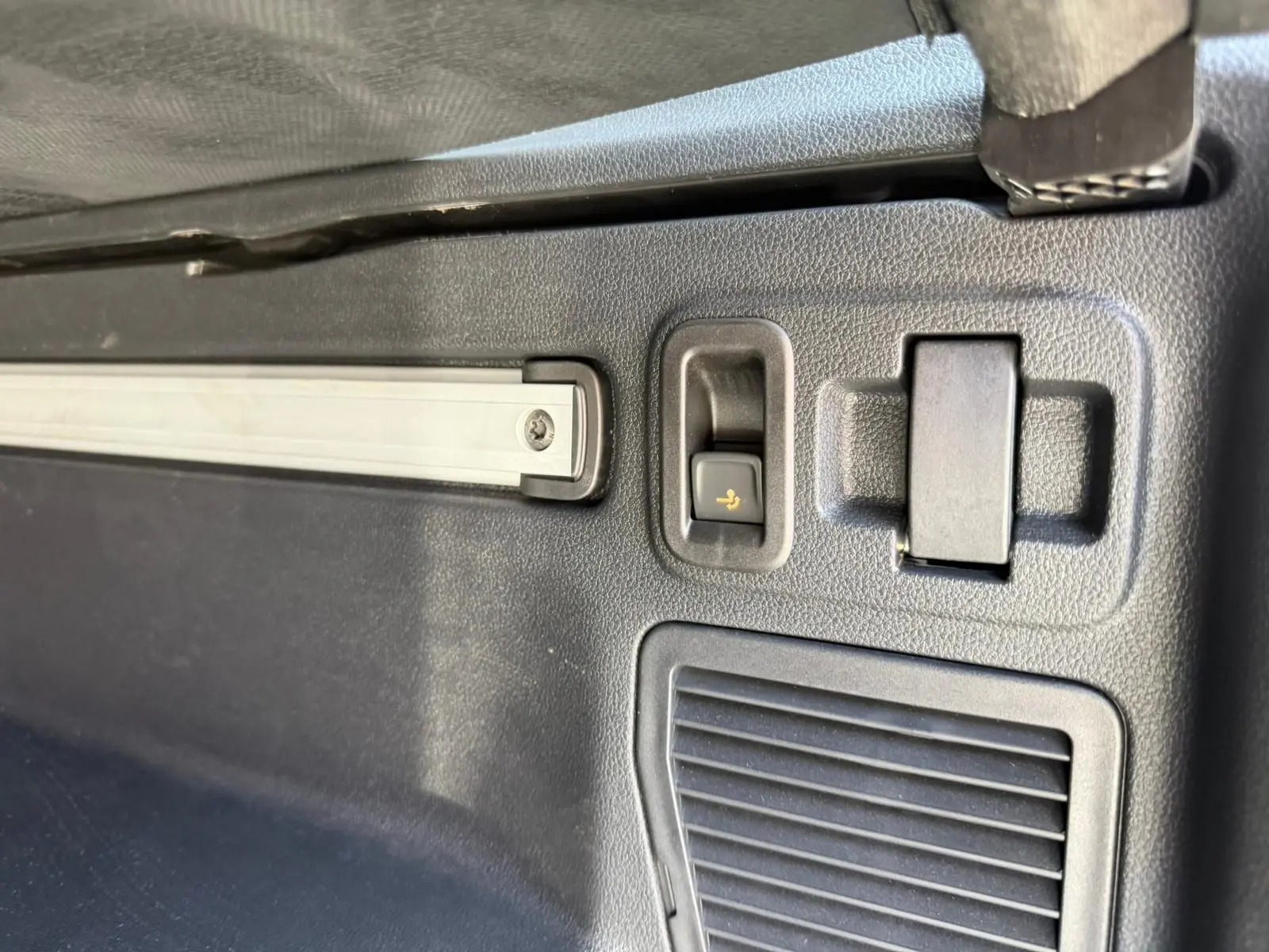 Détail intérieur du coffre du Volkswagen Touran gris, montrant un bouton de rabattement des sièges et une grille d'aération.