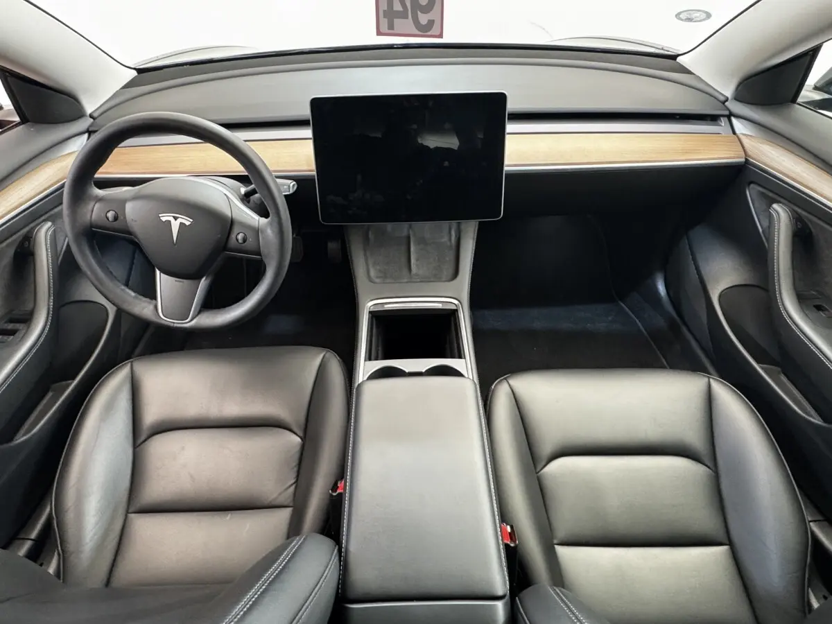Vue intérieure frontale du tableau de bord et des sièges noirs en cuir d'une Tesla Model 3 2023 avec écran tactile central.