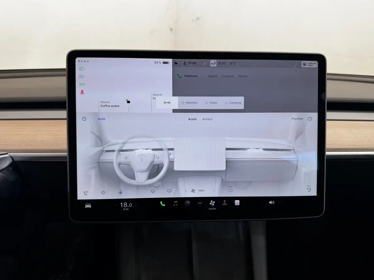 Écran tactile central affichant l’interface de la Tesla Model 3 2023, intérieur bois clair visible en arrière-plan.