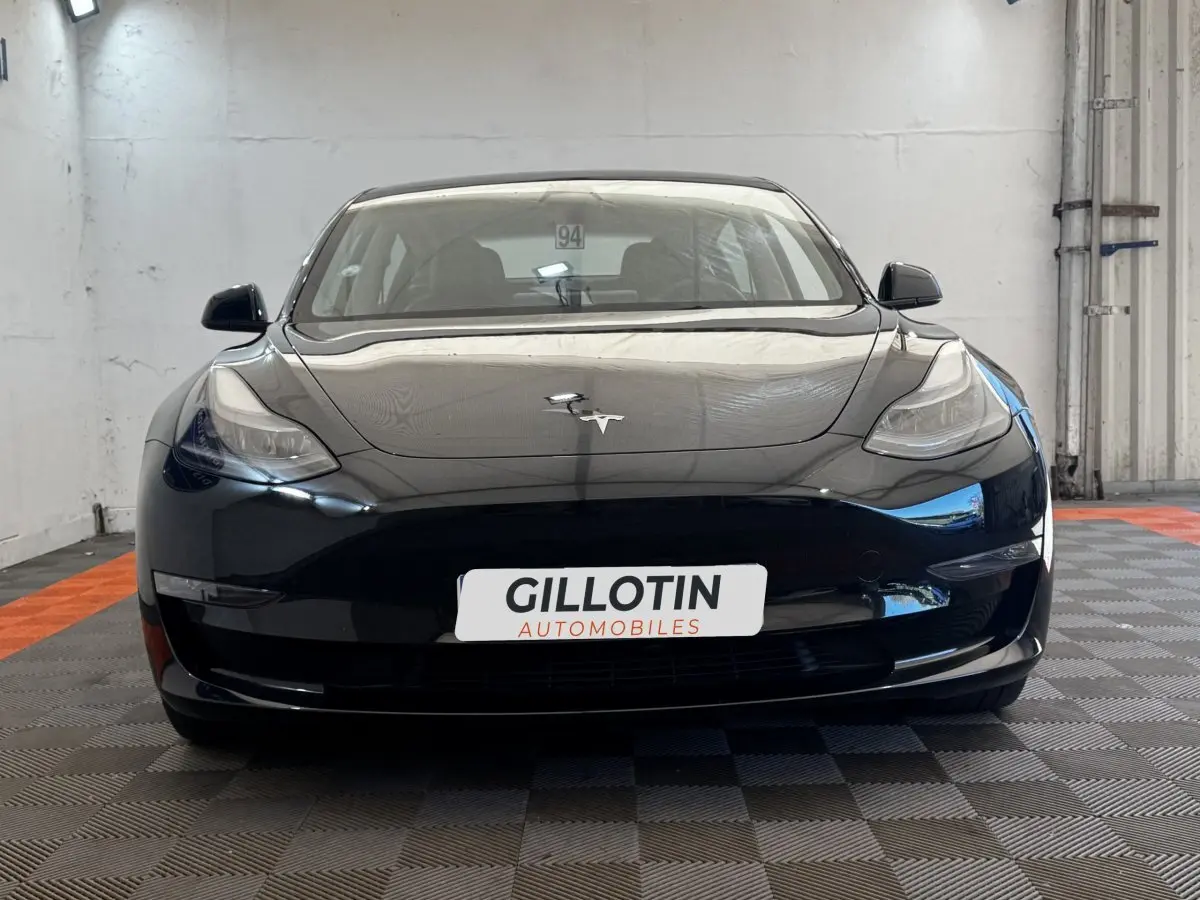 Vue frontale d'une Tesla Model 3 Grande Autonomie noire, avec logo Tesla visible sur le capot lisse.
