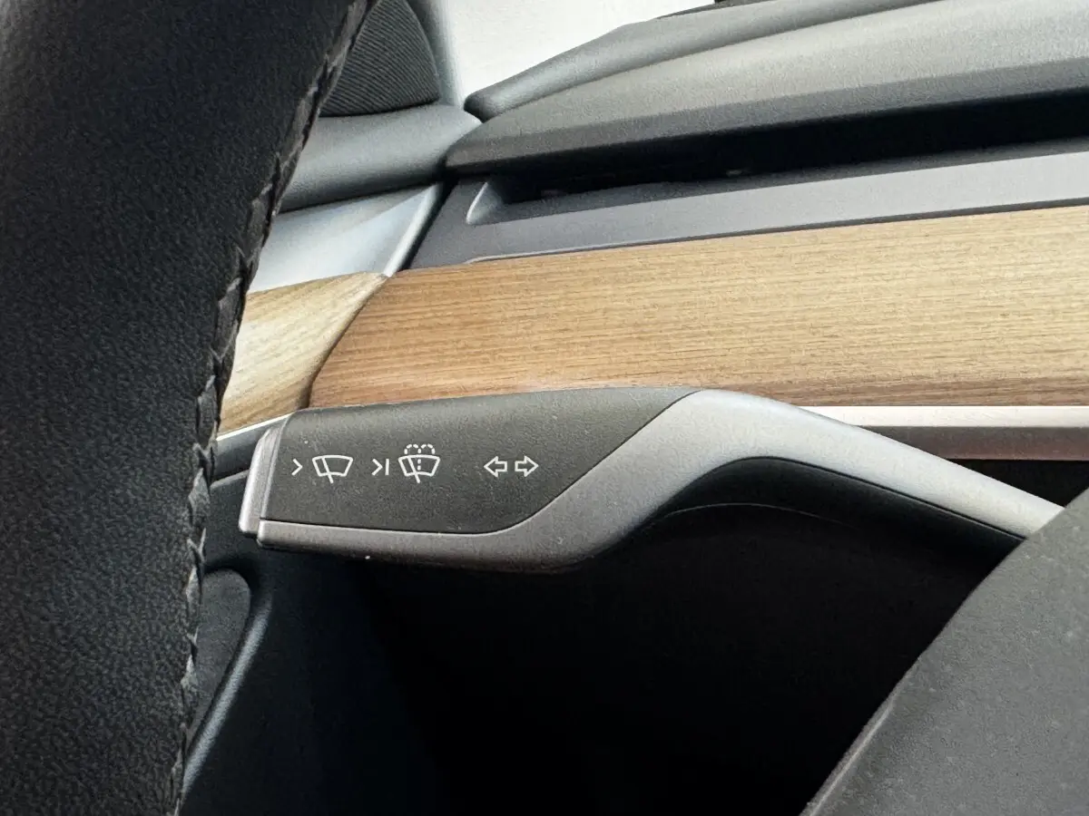 Gros plan sur la commande des essuie-glaces et clignotants dans l’habitacle bois et noir d’une Tesla Model 3 2023.