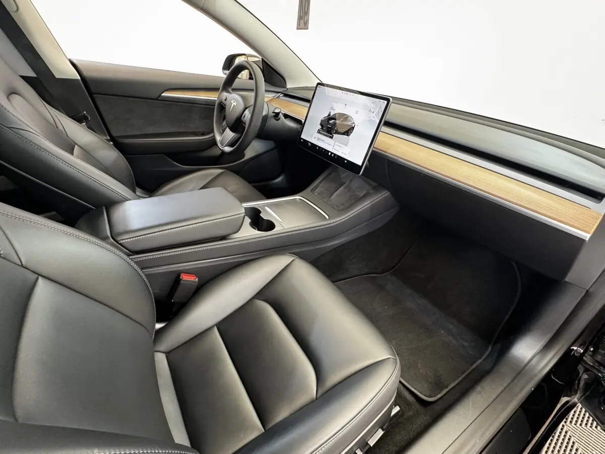Intérieur Tesla Model 3 noir 2023 vu côté passager, avec écran tactile central et tableau de bord bois clair.
