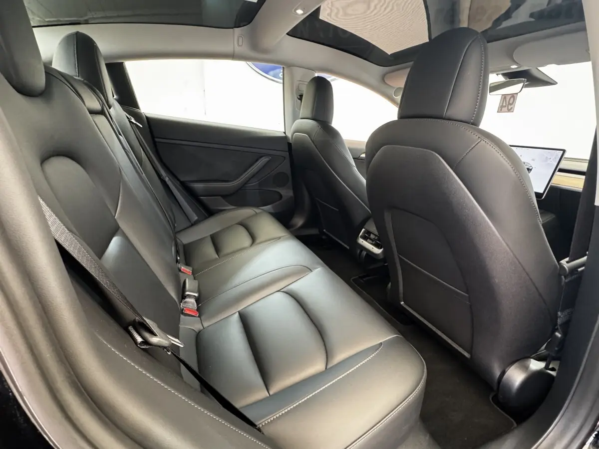 Intérieur arrière de la Tesla Model 3 noire 2023, vue côté gauche montrant les sièges en cuir et le toit panoramique.