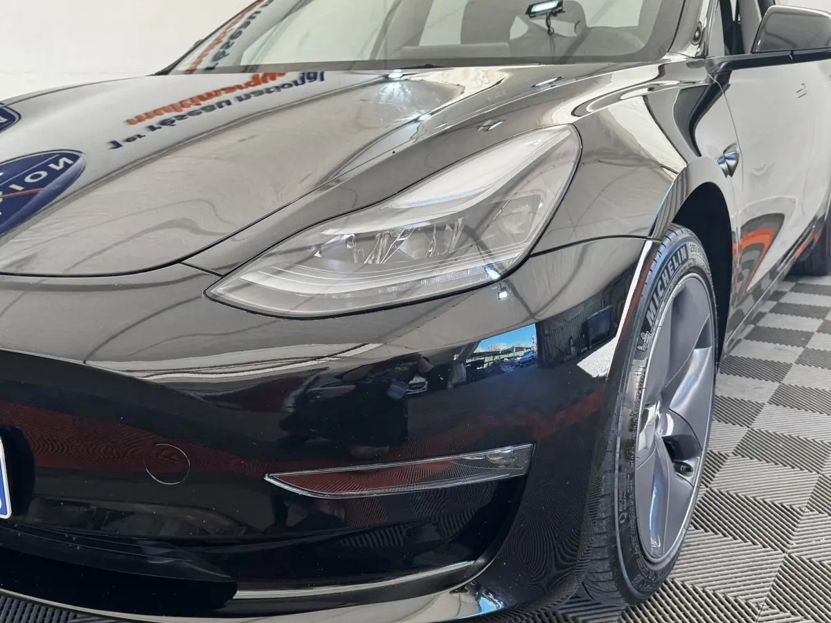 Vue 3/4 avant droit d'une Tesla Model 3 Grande Autonomie noire, mettant en valeur le phare et la roue Michelin.